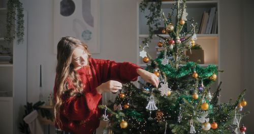 Young woman standing by christmas tree at home