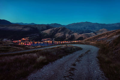 Road leading towards mountains against clear blue sky