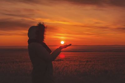 Silhouette woman gesturing while standing on field against orange sky