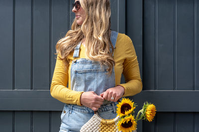 Woman holding yellow flowers in purse against wall