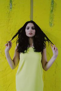 Portrait of beautiful woman standing against yellow wall