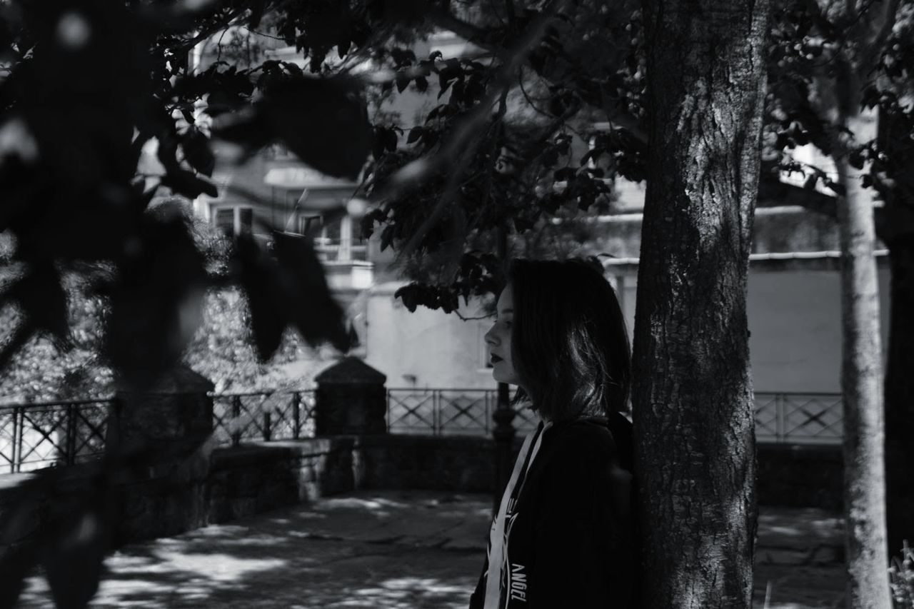 tree, plant, one person, trunk, real people, tree trunk, women, standing, adult, day, lifestyles, focus on foreground, nature, leisure activity, waist up, outdoors, side view, looking, hairstyle