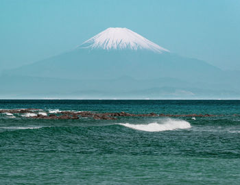 Scenic view of mt. fuji against hazy summer sky and ocean with waves in foreground.