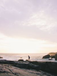 Man on rock by sea against sky