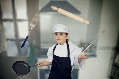 Girl in chef whites playing with cooking utensils