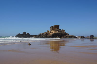 Scenic view of rocks on beach against clear blue sky