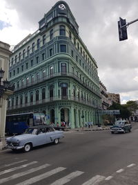 Cars on road by buildings against sky in city