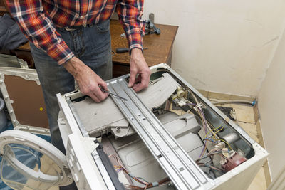 Middle aged man repairing broken washing machine with tools, household chores