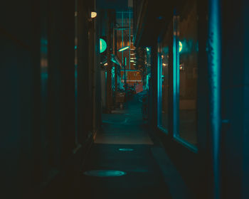 Empty illuminated alley amidst buildings at night