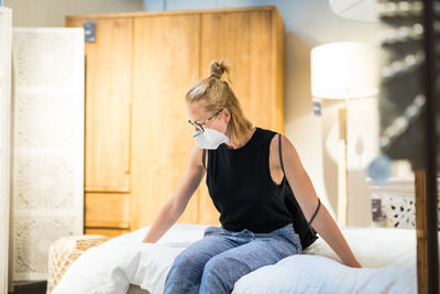 Woman wearing flu mask sitting on bed at store
