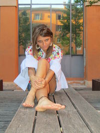 Happy woman sitting on wood against brick wall