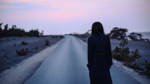 Rear view of woman standing on road against sky during sunset