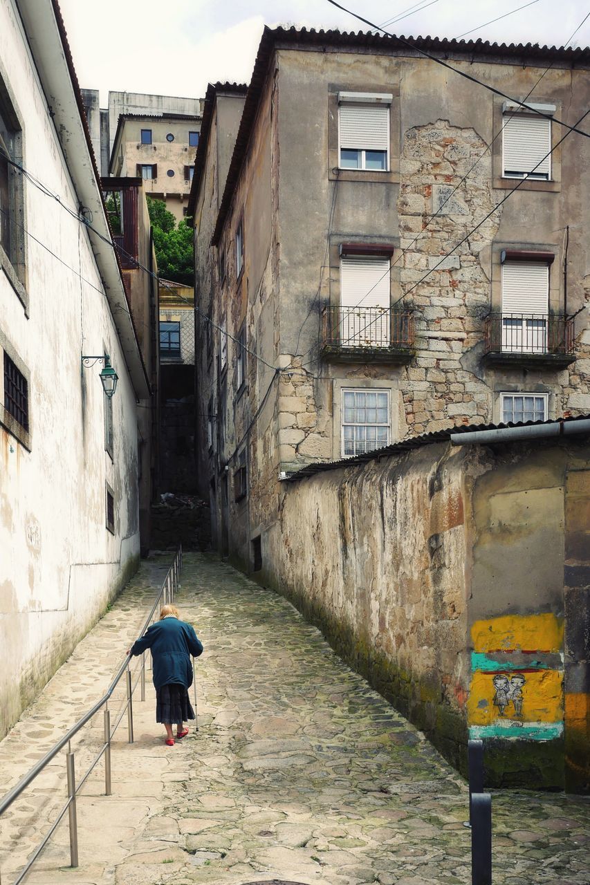 REAR VIEW OF WOMAN WALKING ON FOOTPATH AMIDST BUILDINGS