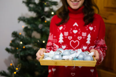 The girl is holding a tray with many decorations on it. the process of decorating a christmas tree