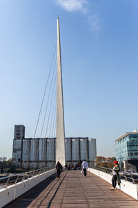 People walking on bridge against sky in city