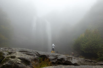 Rear view of man standing on rock against sky