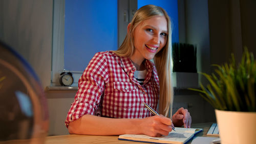 Portrait of young woman writing in book at office