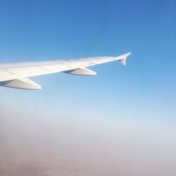 Low angle view of airplane wing against clear blue sky