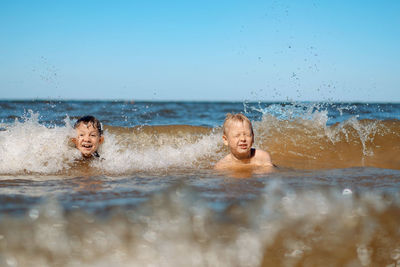 7-8 years old cute caucasian boys swimming in the sea with big splashes in waves