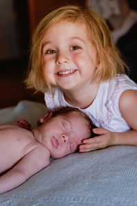 Joyful little crop preschool female touching with interest calm infant with closed eyes resting in bed against blurred interior of light bedroom