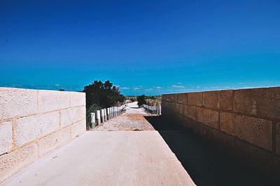 Footpath by wall against blue sky