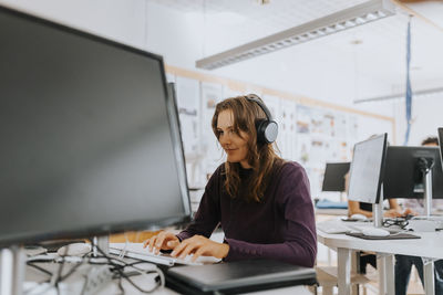 Young woman listening through headphones while using computer in school lab