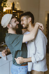 Side view of happy gay couple embracing each other in kitchen at home