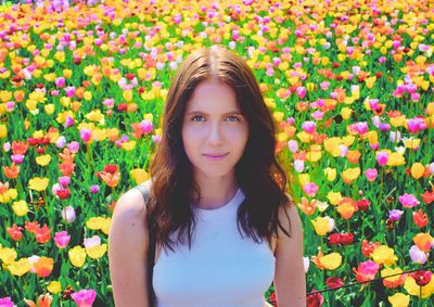 Portrait of beautiful young woman standing against colorful flowers