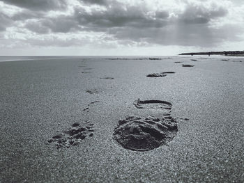 Footprints on sand at beach against sky