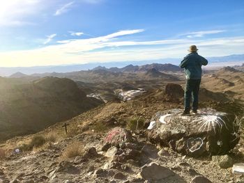 Rear view of man standing on rock against sky