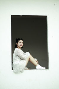 Portrait of young woman sitting against wall