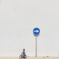 Girl riding tricycle against arrow symbol by wall