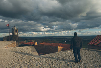 Full length rear view of man standing on building terrace against cloudy sky