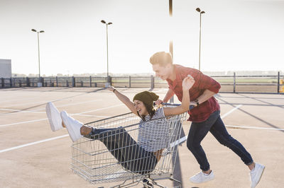 Playful young couple with shopping cart on parking level