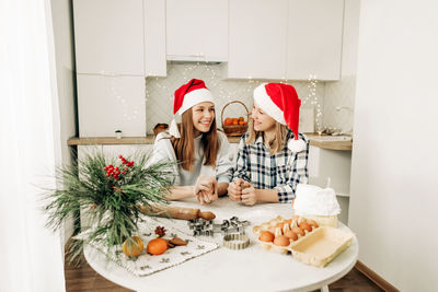 Two charming sisters in santa claus hats bake cookies for christmas in the kitchen. 