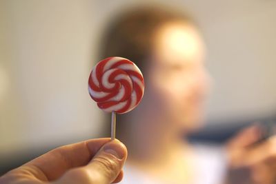 Cropped hand holding lollipop against woman