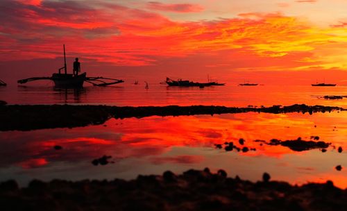 Silhouette boats in sea against orange sky