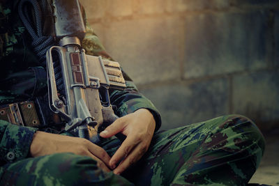 Midsection of army soldier sitting with weapon
