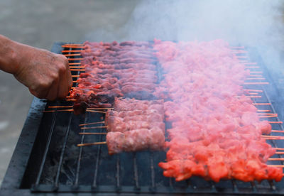Person holding meat on barbecue grill