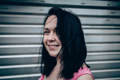 Close-up of smiling young woman standing against shutter