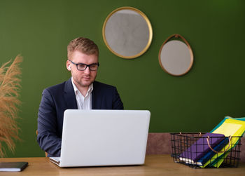 Blond caucasian business man with glasses with headphones working at laptop in office or at home