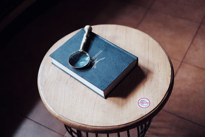 High angle view of book and magnifying glass on table at home