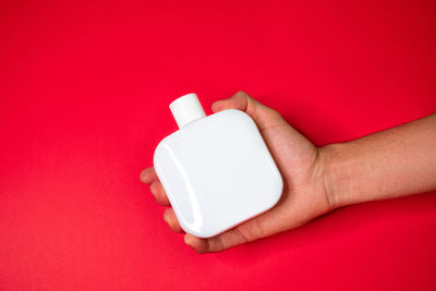 Close-up of hand holding red rose over colored background