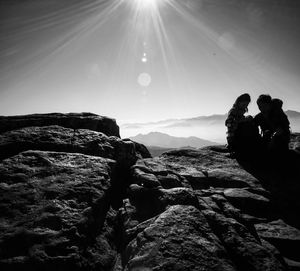 Hikers sitting on rock against bright sky