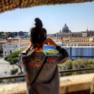 Rear view of woman photographing city against sky