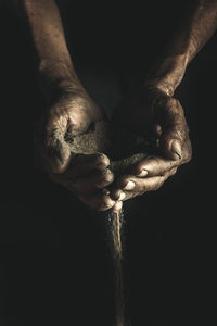 Cropped hands of man holding sand against black background