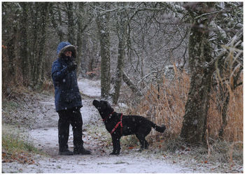 Woman standing with dog in forest during snowfall