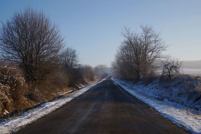 Road amidst bare trees against sky during winter