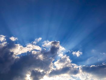 Low angle view of sunlight streaming through clouds