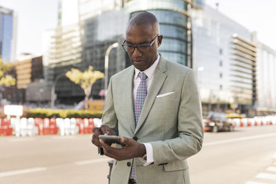 Mature businessman using smart phone on street at financial district